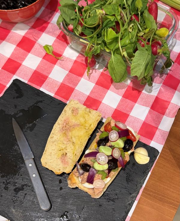 An open-faced sandwich with sliced vegetables and cheese sat on a black cutting board next to a small kitchen knife