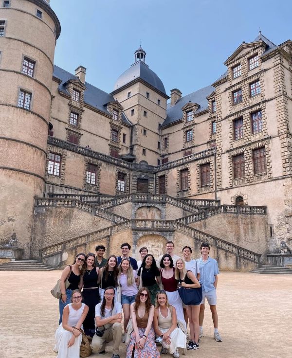 A group of study abroad students smiling at the camera in front of a large ornate stone building