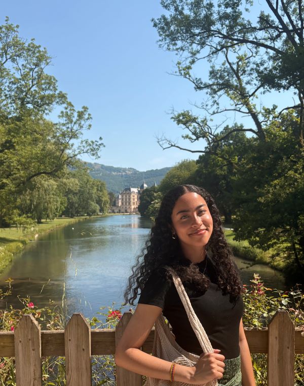 A study abroad student standing in front of a body of water and smiling at the camera