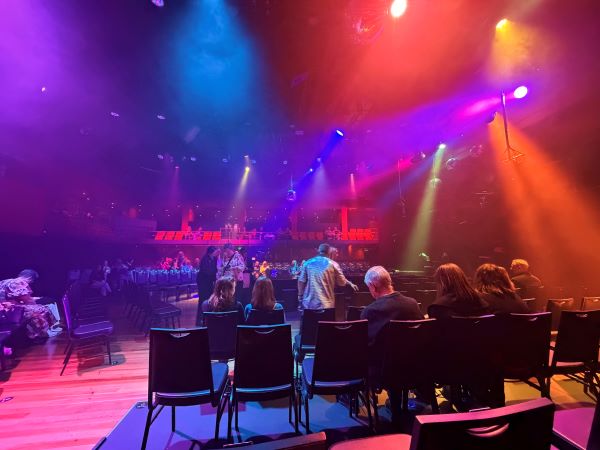 An indoor performance space full of people sitting in chairs and bathed in brightly colored lights from above