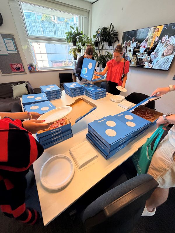 A group of study abroad students opening blue pizza boxes sitting on an indoor table