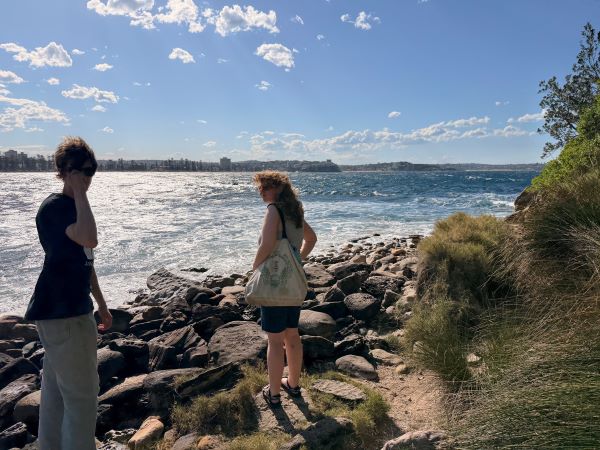 Two study abroad students standing outdoors in front of a rocky shoreline with a large body of water in the background