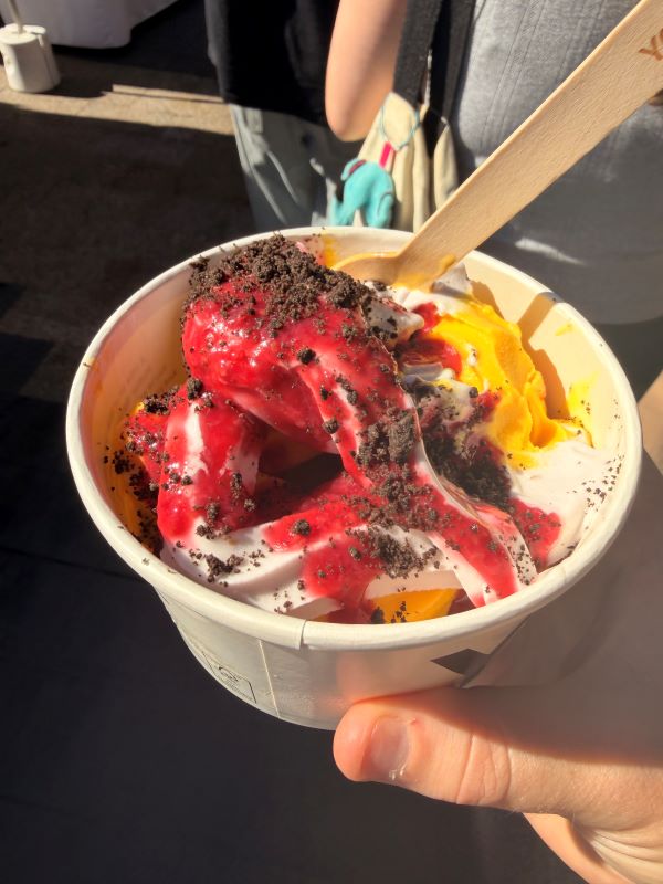 A paper bowl of brightly-colored red and yellow frozen yogurt covered in chocolate sprinkles