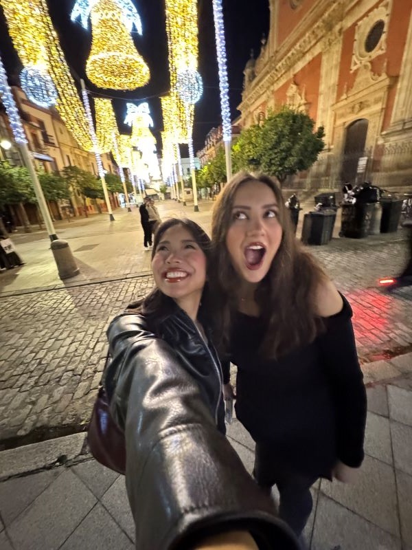 Two study abroad students taking a selfie in an outdoor space at night in front of bright lights