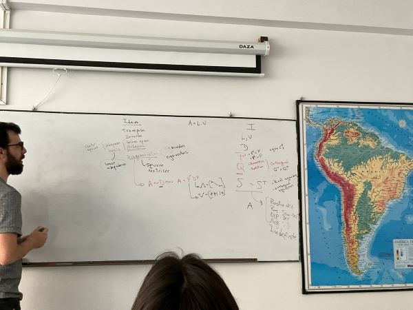 A person standing to the left of a classroom whiteboard that is covered in written equations