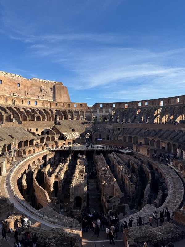 The interior of the Roman Colosseum as seen from a height, featuring many people walking among its stone ruins