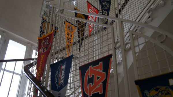 A stairway bannister, as seen from below, draped with small pendant flags from various US universities