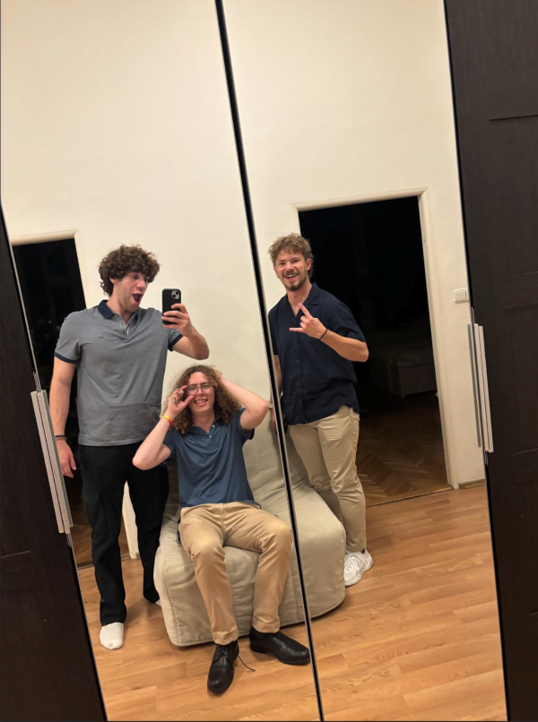 Three study abroad students all wearing blue polo shirts taking a selfie in a mirror indoors and smiling at the camera