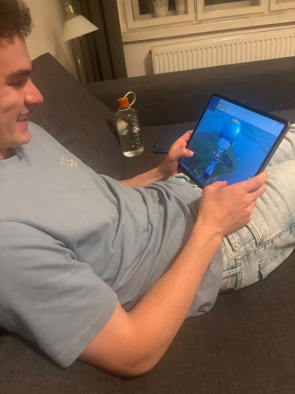 A study abroad student sitting on a couch and smiling down at a computer tablet while playing a game on it
