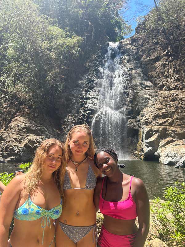 A group of study abroad friends posing for a picture in front of a waterfall
