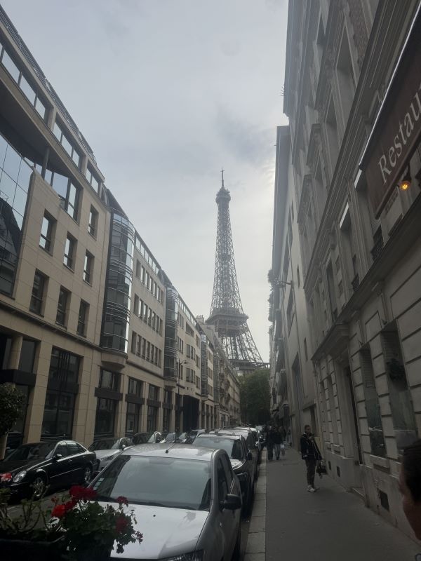 A city street full of parked cars with the Eiffel Tower standing at the end of it