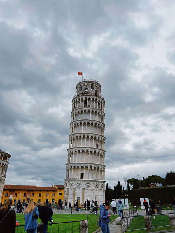 A tall leaning tower with a flag on top with Leaning Tower of Pisa in the background