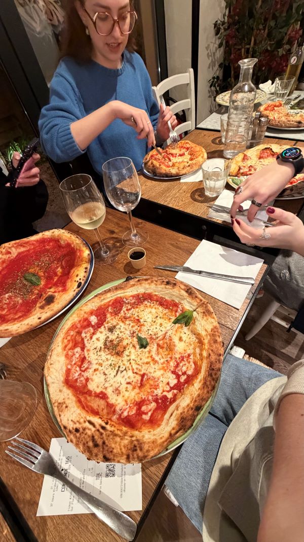 A group of study abroad students sitting at a table on which several large pizzas sit