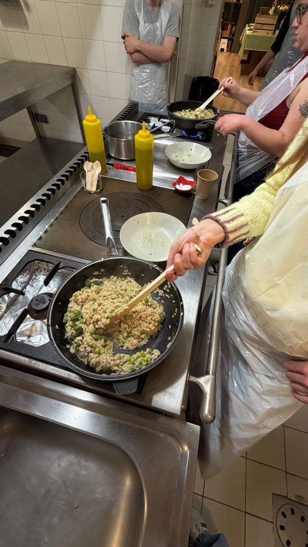 The arm of a study abroad student is seen stirring a mix of rice in peas in a pan on a stove