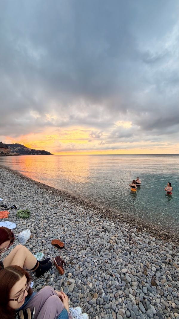 A group of study abroad students at the beach - some seated on the rocky shore and some standing in the shallow water