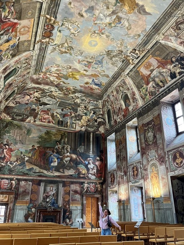 A study abroad student standing inside an intricately decorated space and smiling at the camera with their arms spread wide