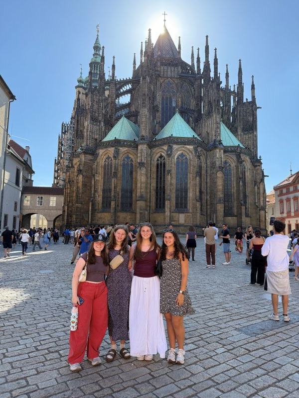Four study abroad students standing outdoors in front of a large cathedral and smiling at the camera