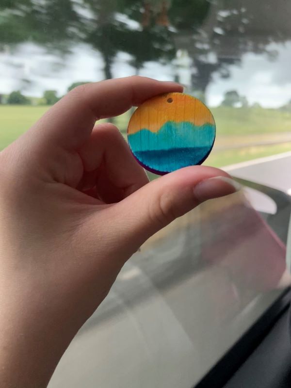 A study abroad student's hand holding up a small circular wooden pendant painted yellow and blue