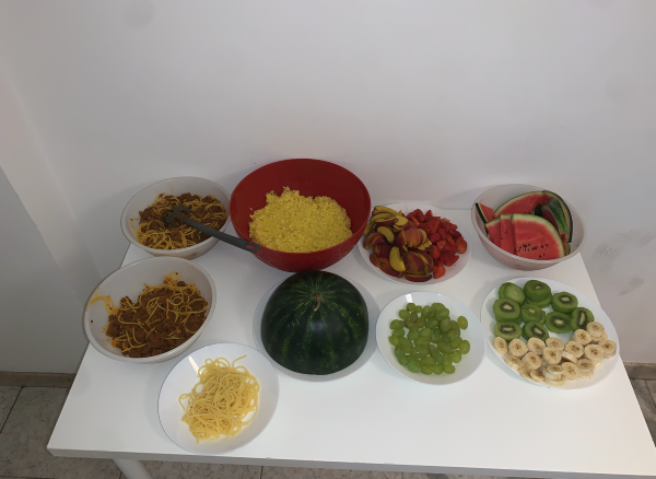A white table in an indoor setting laden with many plates of food, including pasta, fruit, and vegetables