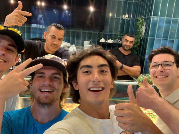 Four study abroad students smiling and taking a selfie with two people standing behind a counter