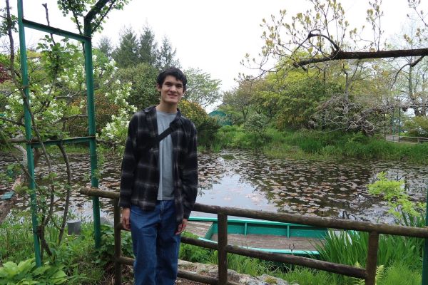A study abroad student standing in front of a small body of water and smiling at the camera