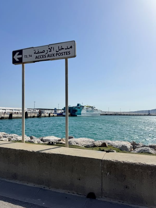 A body of water with a boat in the distance and a sign with writing in Arabic close to the viewer