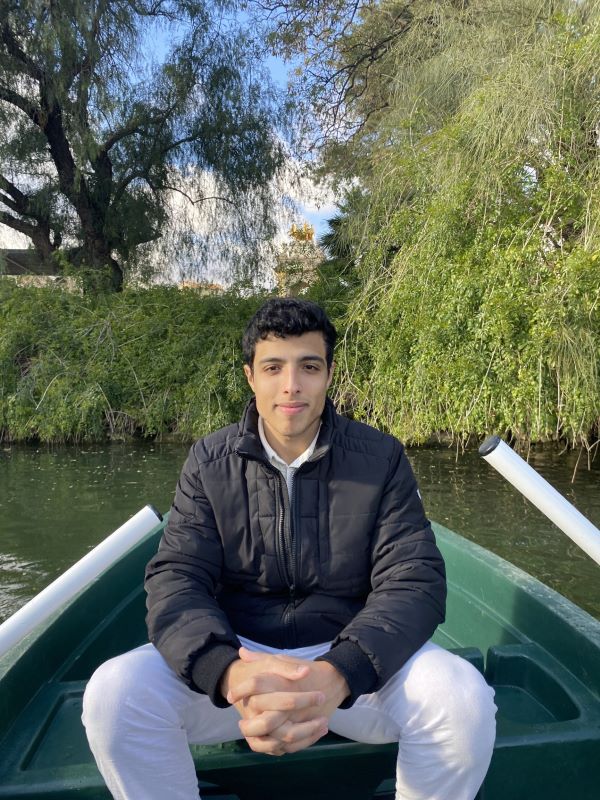 A study abroad student sitting in a small green rowboat with their hands folded together and smiling at the camera