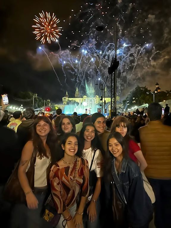 A group of study abroad friends smiling at the camera during nighttime with a crowd and fireworks in the background