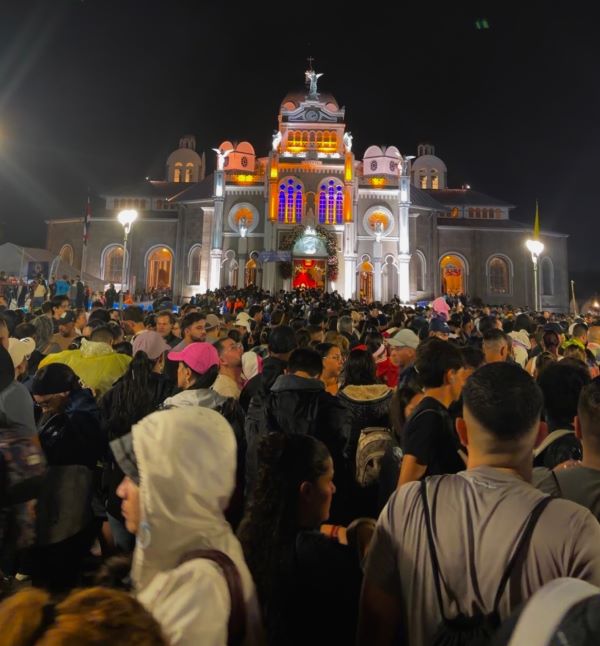 A large white building with brightly colored windows seen at night with a large crowd of people standing in front of it