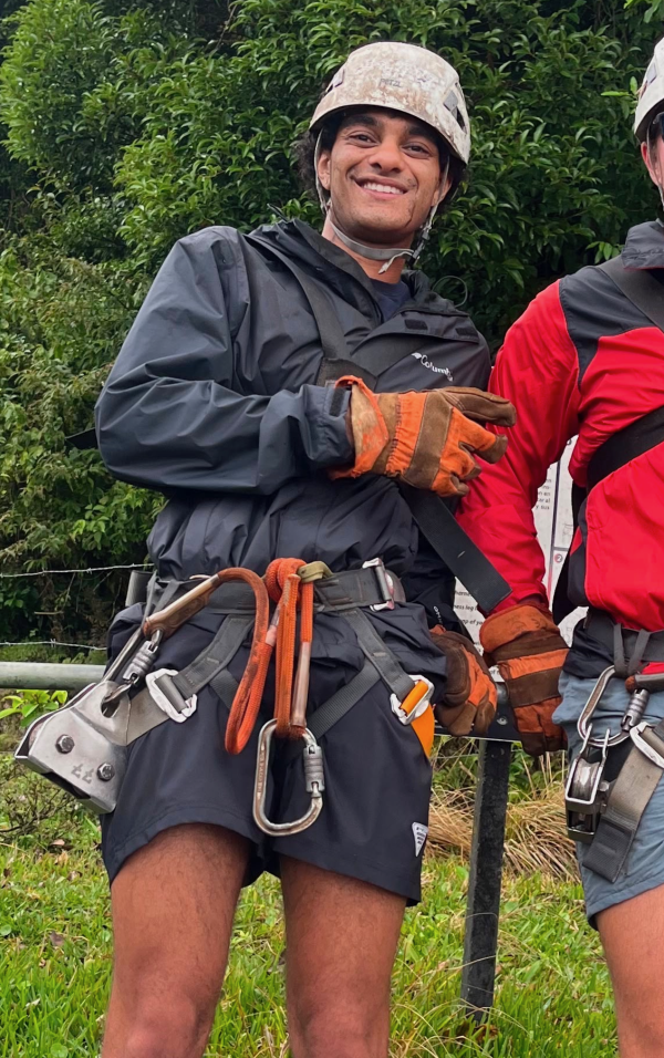 A study abroad student standing outdoors, wearing a helmet and large metal belt and smiling at the camera