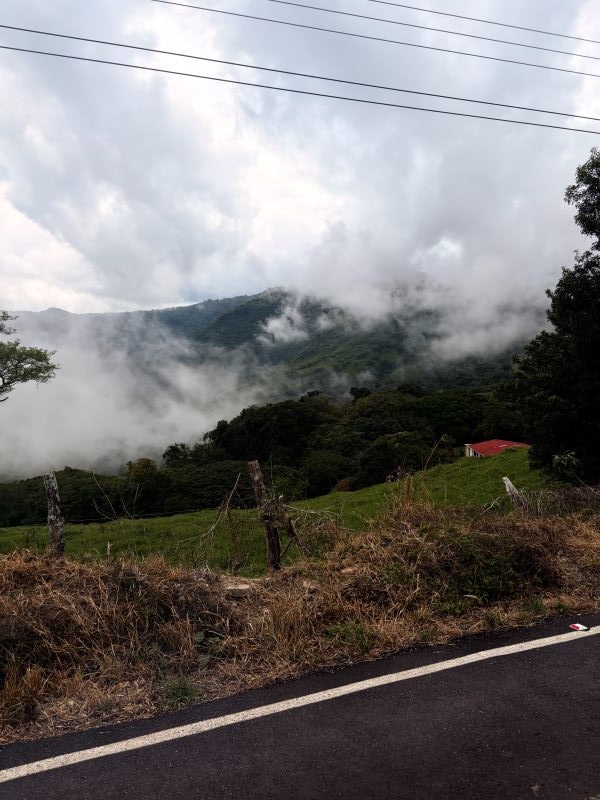 A large green mountain engulfed in clouds of fog, seen from a nearby road
