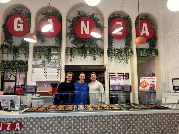 Two study abroad students posing for photo with pizza shop owner in store