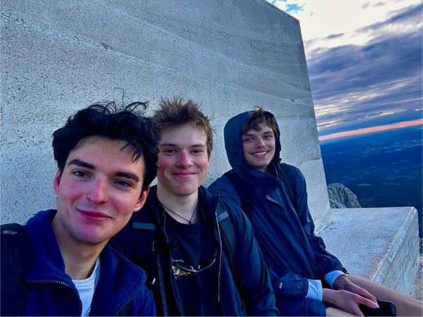 Three study abroad students sitting on an outdoor stone bench and smiling at the camera