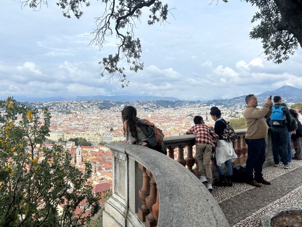 A person seen from the side looking out over a stone balcony onto a mountainous cityscape below