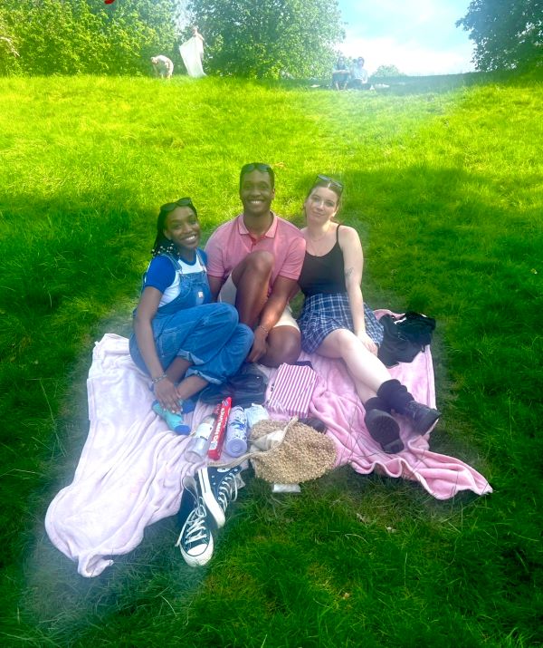 Three study abroad students sitting together on blankets in the grass and smiling at the camera
