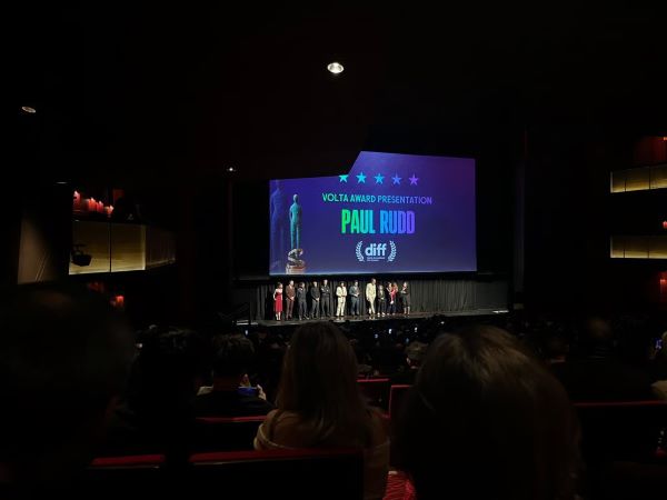 A far-away shot of a group of people standing on a stage under a large screen