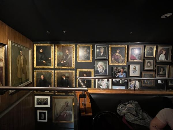 A wall in an indoor space featuring many framed photos and portraits of various people