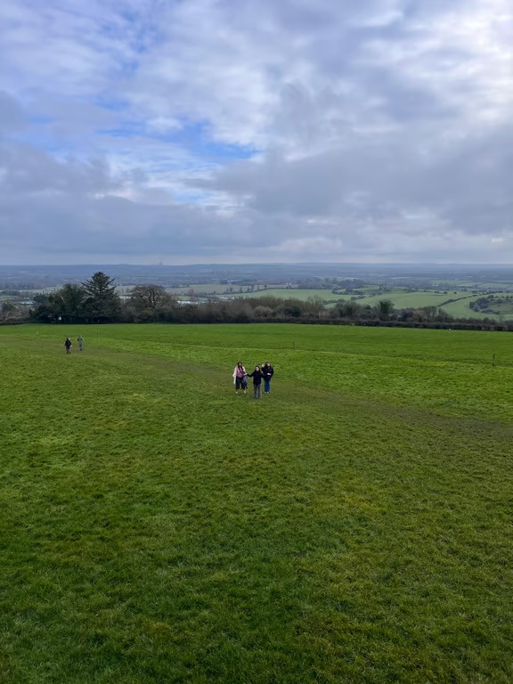 A group of study abroad students as seen from a distance walking through a vast green landscape under a cloudy sky