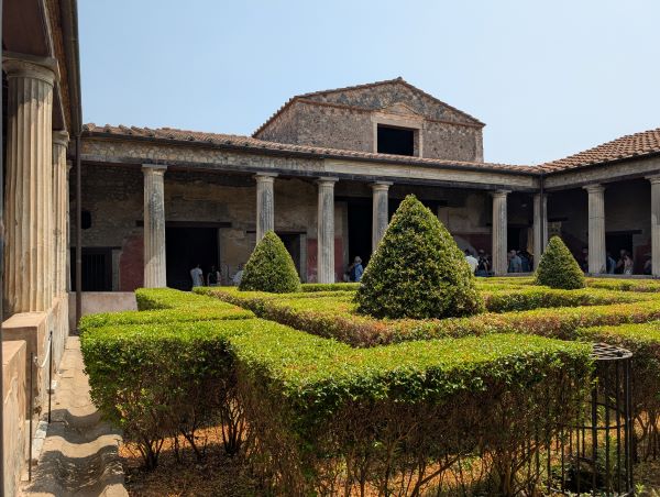 A stone building featuring a small courtyard full of small trees and bright green hedges