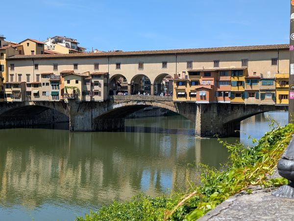 A bridge featuring small individual buildings suspended over a body of water under a bright blue sky
