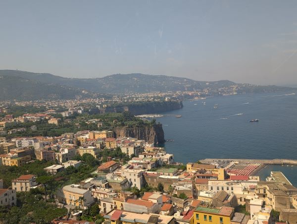 A view from above of multicolor stone buildings lining a body of water with low green mountains in the background