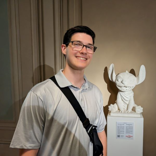 A study abroad student standing indoors and smiling at the camera in front of a small white statue of a friendly alien