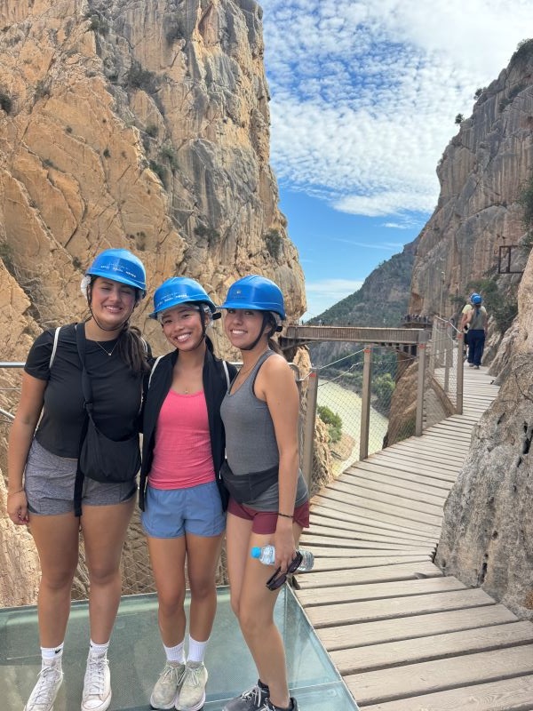 Three study abroad students wearing blue helmets in an outdoor setting and smiling at the camera