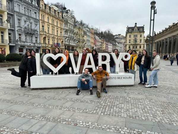 A group of study abroad students standing by a large sign and smiling at the camera