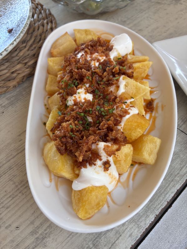 A white dish full of small crispy fried potatoes covered in a white sauce and crispy brown meat crumbles