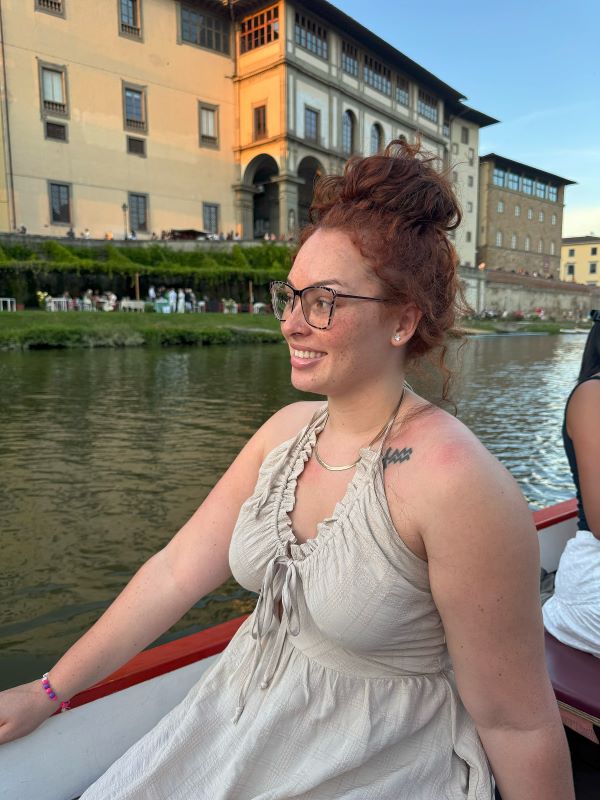 A study abroad student sitting in a boat in a small river and smiling while looking away from the camera
