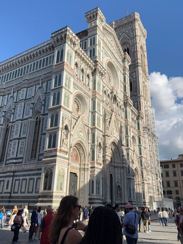 People walking around outside a large intricately designed white building under a blue sky
