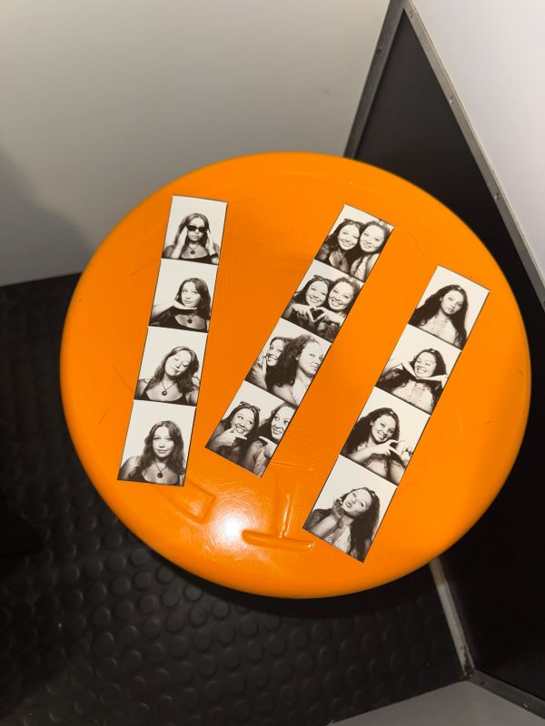 Three strips of black-and-white photo booth photos laid on a small round orange table