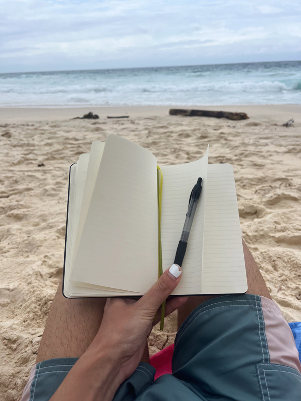 A study abroad student holding a notebook and a pen on a beach