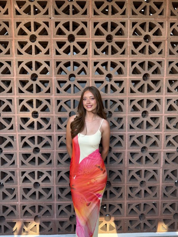 A study abroad student wearing a white dress with a bright flower pattern on it and smiling at the camera